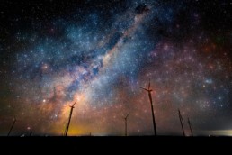 Windkraftanlagen bei Nacht vor funkelndem Sternenhimmel