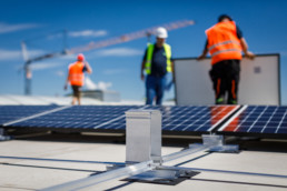 Installers latch solar modules into a pre-assembled substructure on a large flat roof.