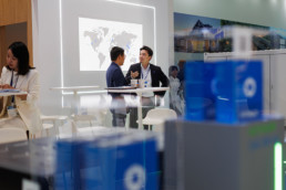 Two Asian people in conversation, blurred blue batteries in display cases in the foreground